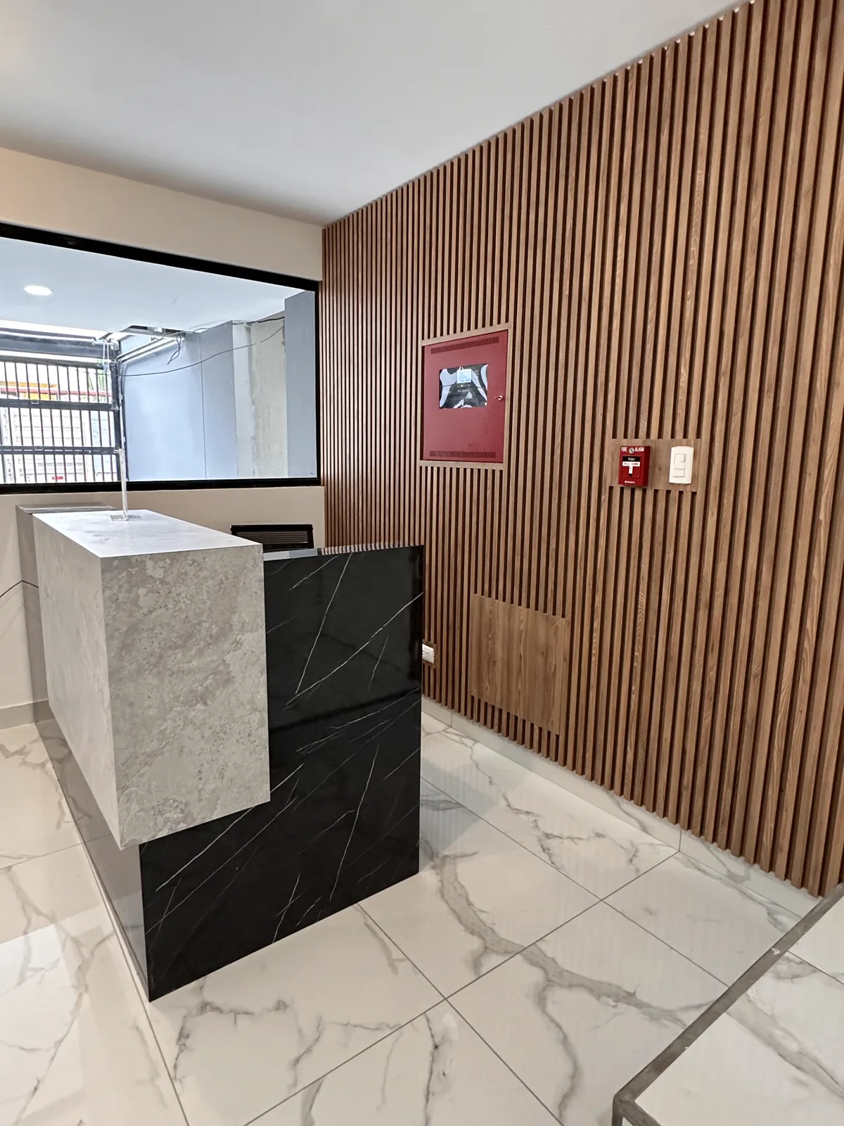Recepción con panel de listones de madera y mesón de mármol del proyecto Dalias